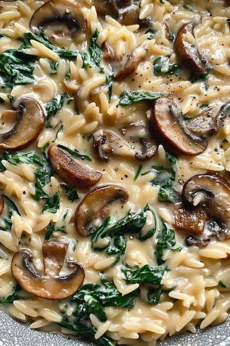 Creamy spinach mushroom orzo dish garnished with fresh herbs.